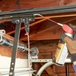 Homeowner applying white lithium grease to garage door hinges during routine maintenance