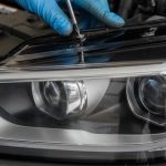 Driver turning horizontal adjustment screw on car headlight assembly at night