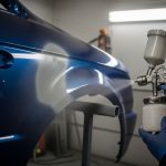 Budget HVLP paint sprayer applying automotive primer to car panel in home garage