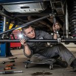 Mechanic inspecting suspension and steering components under a lifted vehicle